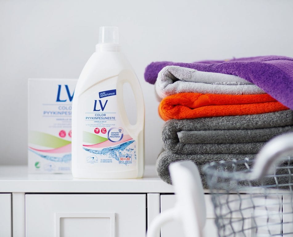 Kuva kodinhoitohuoneen tasosta, jonka päällä värikkäitä pyyhkeitä taiteltuina. Niiden vieressä LV Color pyykinpesuneste ja pyykinpesujauheiden pakkaukset.