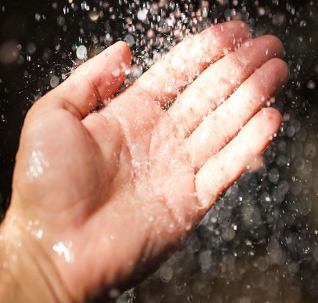 Käsi, jonka ympärillä roiskuvaa vettä kirkkaassa valossa.